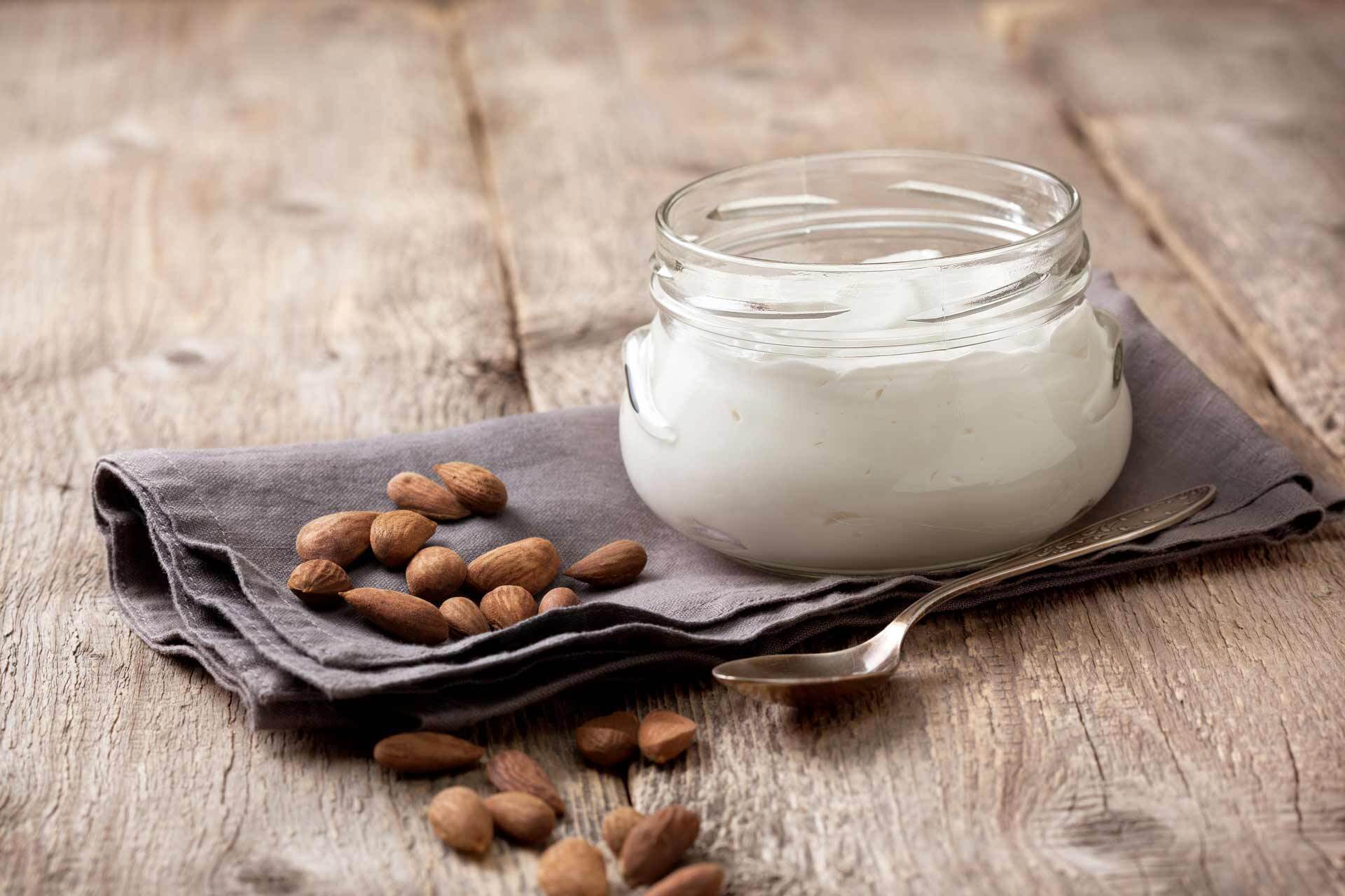 Bowl of almond yogurt next to scattered whole almonds, a napkin & a spoon