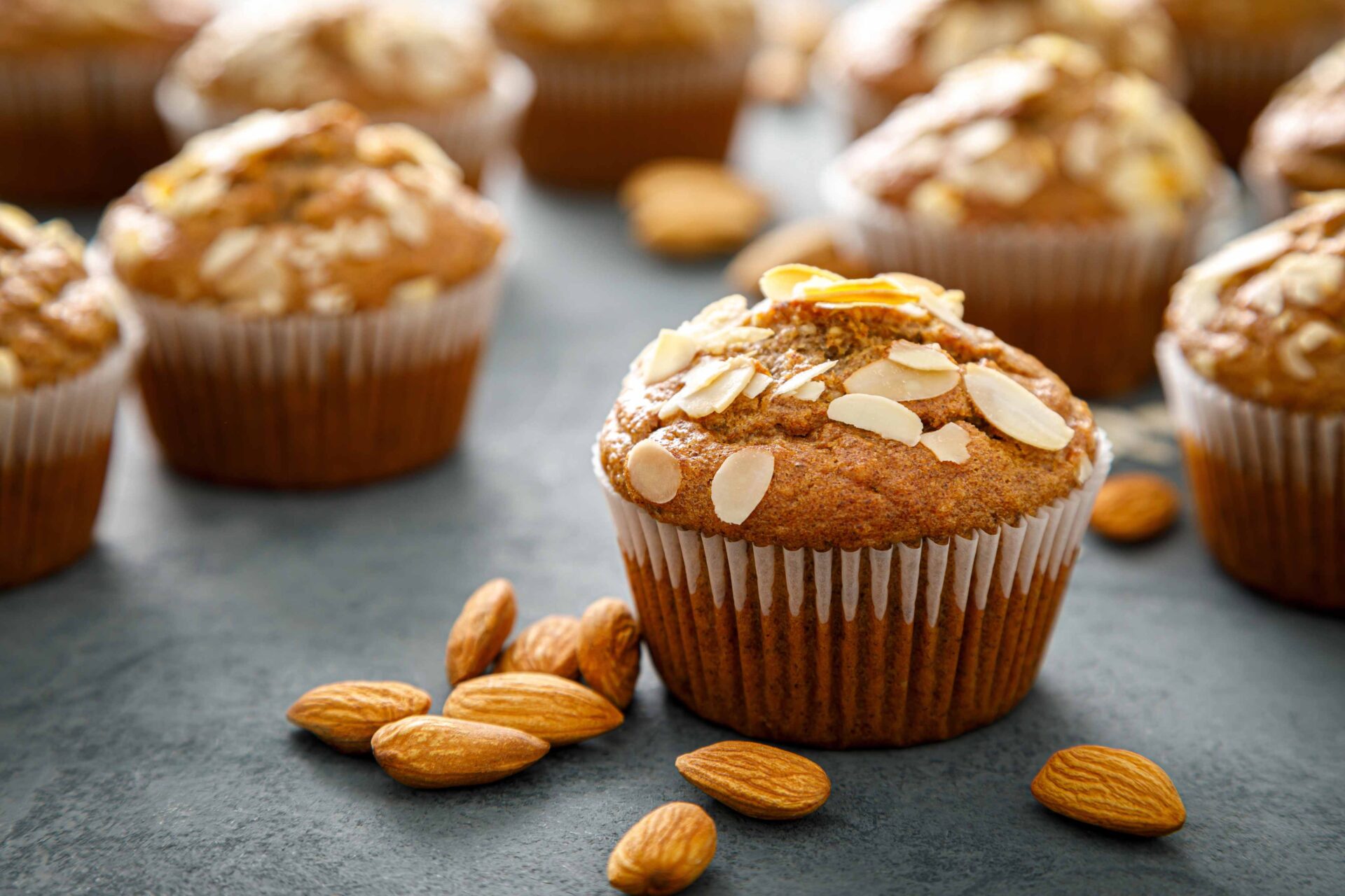 Muffin with Sliced Almonds on top next to scattered raw whole almonds