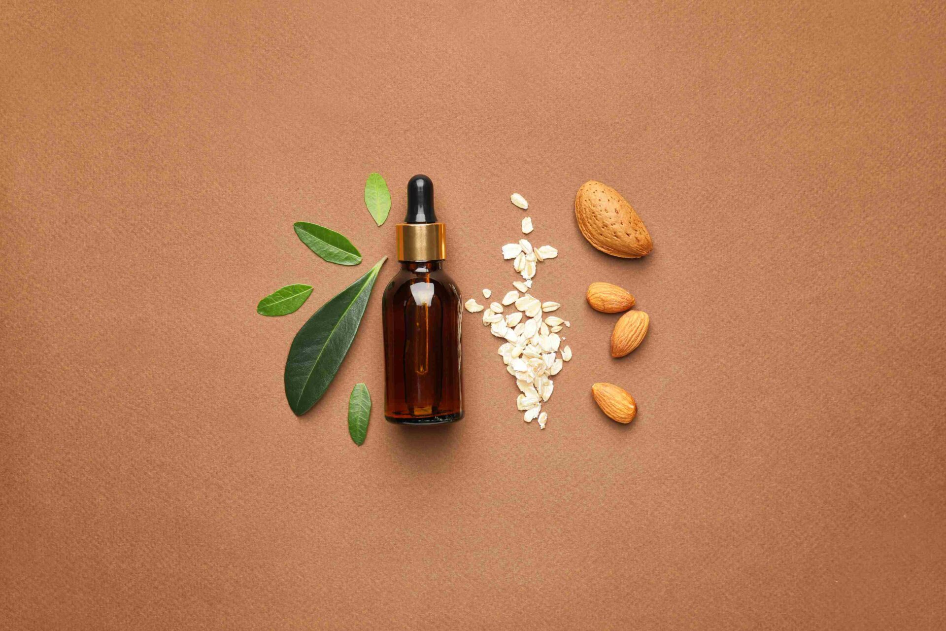 A Bottle of Almond Oil Face Serum Lined up Next to Leaves and Almonds - Almond Oil in Cosmetics and Beauty Products