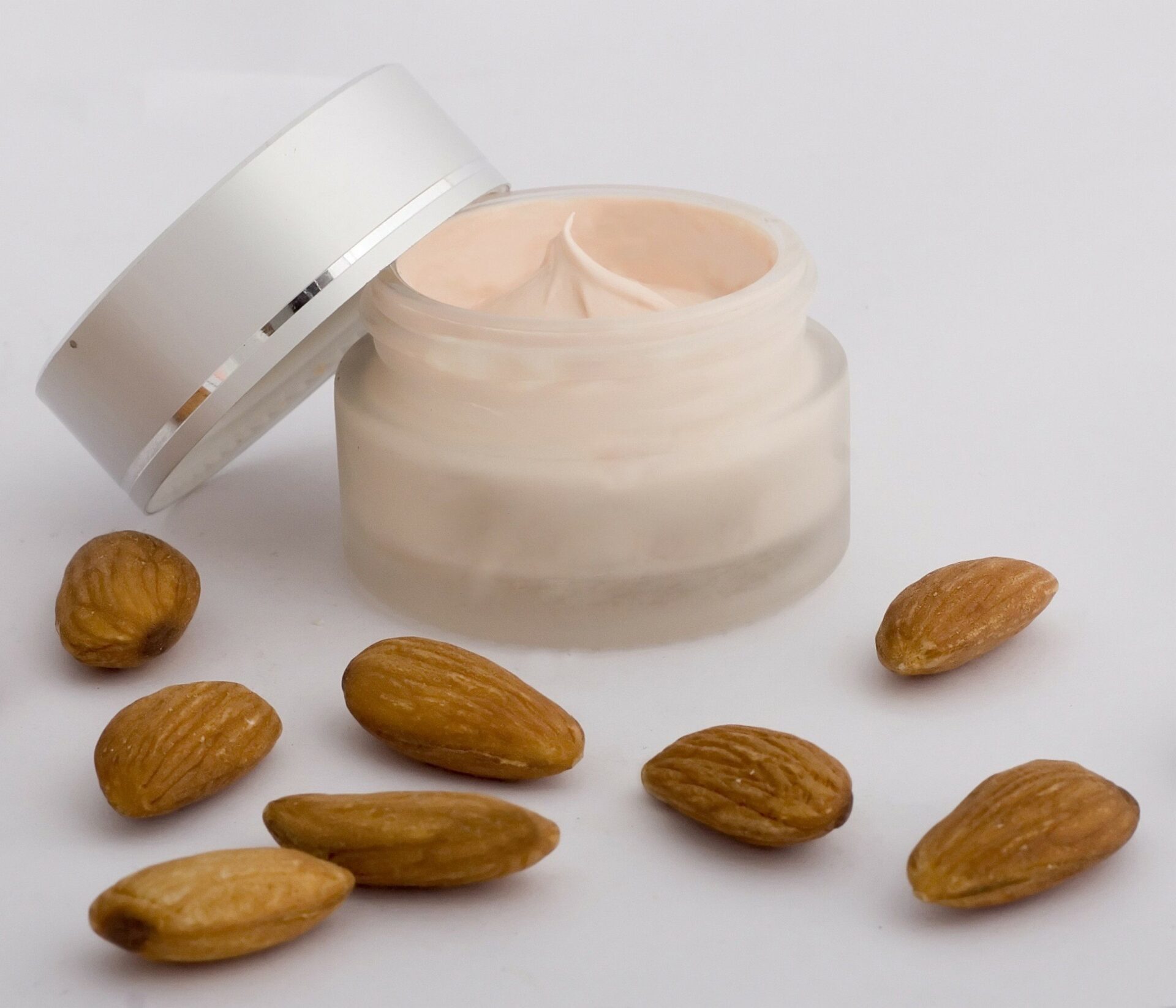 A Container of Almond Oil Skin Cream with Whole Almonds sitting in Front - Almond Oil in Cosmetics and Beauty Products