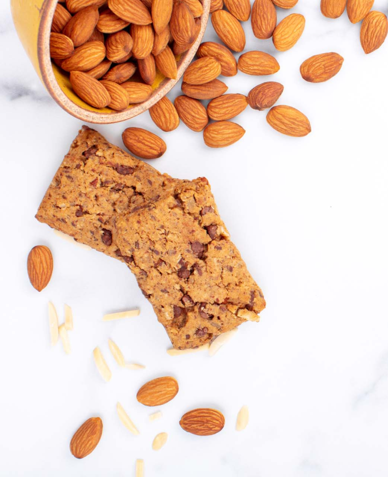 Almond butter nutrition bars next to a bowl of raw whole almonds