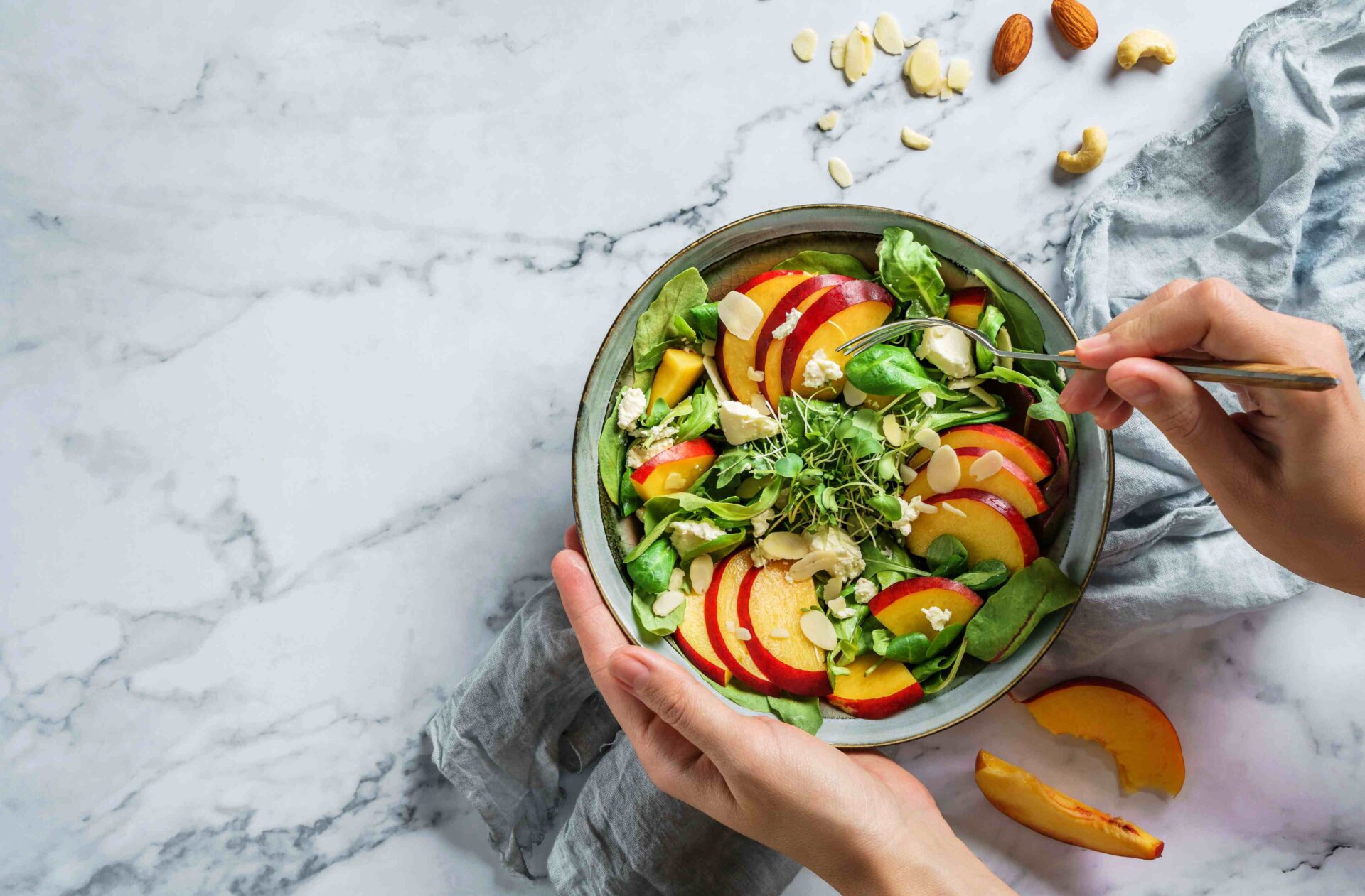 A bowl of salad with Sliced Almonds and nectarine slices on top