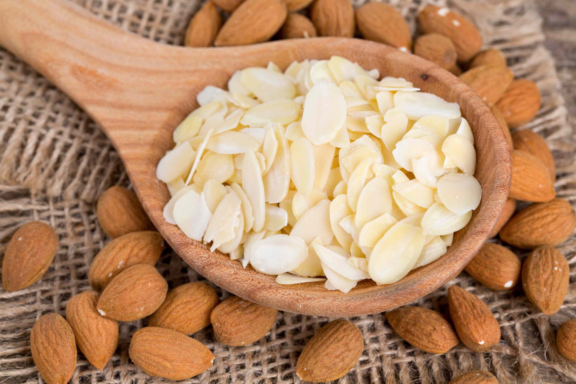 Sliced almonds in a spoon next to raw whole almonds